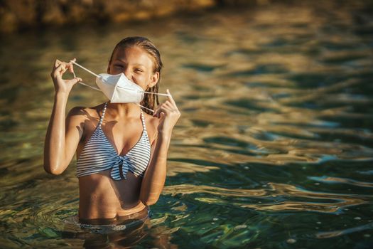 Shot of an happy teenager with surgical mask enjoying a vacation on the beach during the COVID-19.