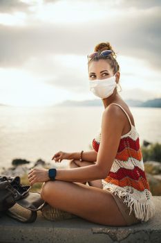 Shot of a happy young woman with protective mask spending time on seaside during exploring a Mediterranean at corona pandemic. 