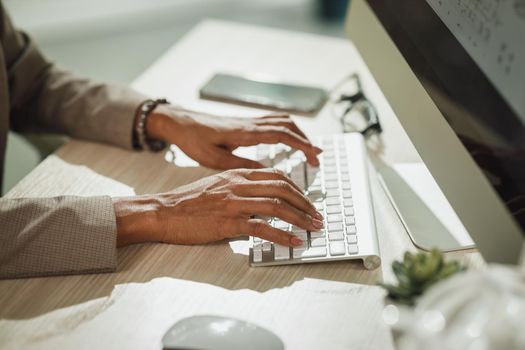 Cropped shot of a hands of African businesswoman sitting alone in her office and using keyboard while working on computer during corona virus pandemic.
