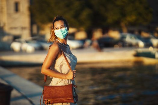 Shot of an attractive young woman wearing a surgical mask while enyoing herself during walk promenade by the sea.