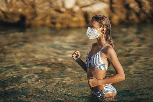 Shot of an happy teenager wearing surgical mask enjoying a vacation on the beach during the COVID-19.