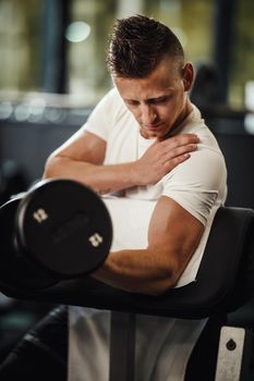 Shot of a muscular guy in sportswear working out at the hard training in the gym. He is pumping up biceps muscule with heavy weight.