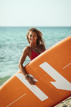 Portrait of a beautiful young female surfer is standing on the beach.