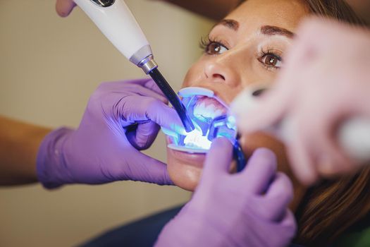 Cropped shot of a beautiful young woman is at the dentist. She sits in the dentist's chair and the dentist fixed lingual locks on her teeth with curing light.