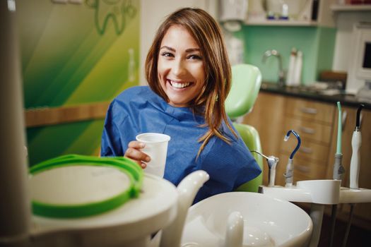Shot of a beautiful young woman is at the dentist. She sits in the dentist's chair and looking at camera after being examined by a dentist.