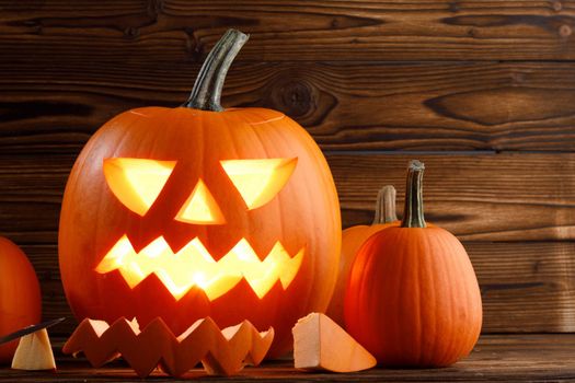 Carved halloween pumpkin with burning candle inside on wooden backdrop