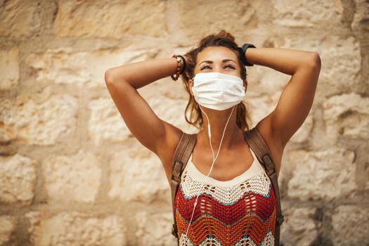 Shot of a happy young woman with protective mask spending time on vacation and having fun during exploring a Mediterranean city at corona pandemic. 