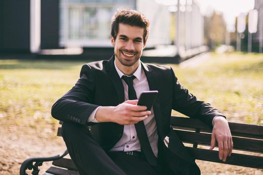 Elegant businessman using phone while sitting outdoor.Toned image.