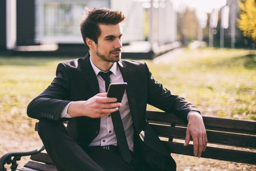 Elegant businessman using phone while sitting outdoor.Toned image.