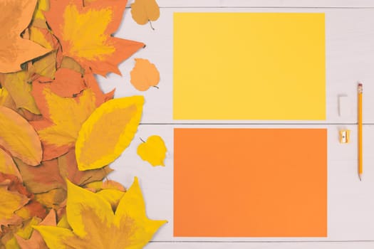 Empty colored papers and school supplies on wooden table with painted leaves.Toned image.