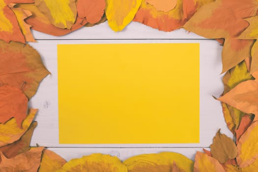 Empty yellow paper on wooden table surrounded with painted leaves.Toned image.