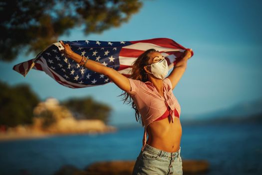 Attractive young woman with US national flag and protective N95 mask on the beach during preventing the spread of the epidemic and treating coronavirus and pandemic COVID-19.