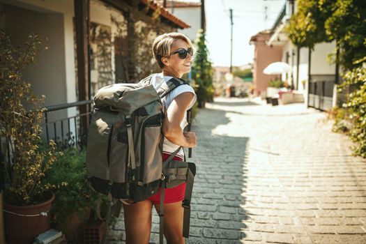 A beautiful young tourist arrived in a Mediterranean city with a backpack on her back. She is enjoying in summer sunny day.