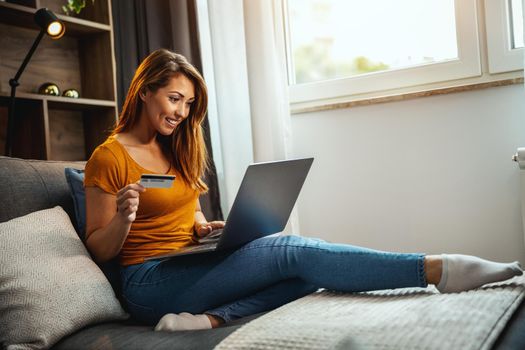 Shot of a cute young woman doing online shopping on her laptop while sitting on the sofa at home.