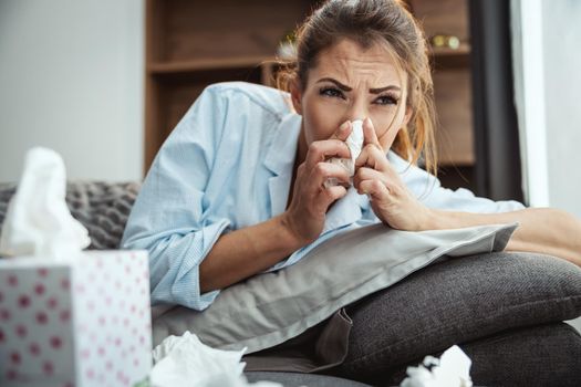 Young woman is lying sick at home couch blowing nose with handkerchief.