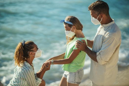 Shot of a happy family with protective N95 mask spending time on the seashore at corona pandemic. 