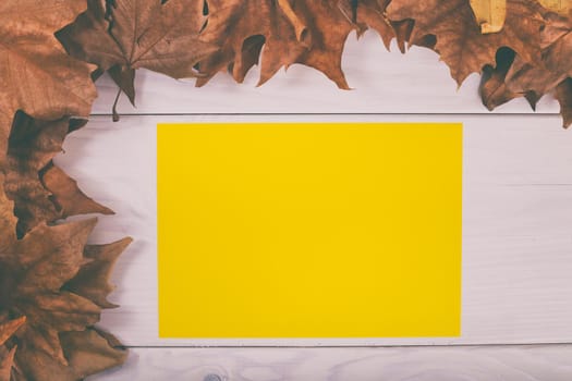 Empty yellow paper on wooden table with autumn leaves.Image is intentionally toned.