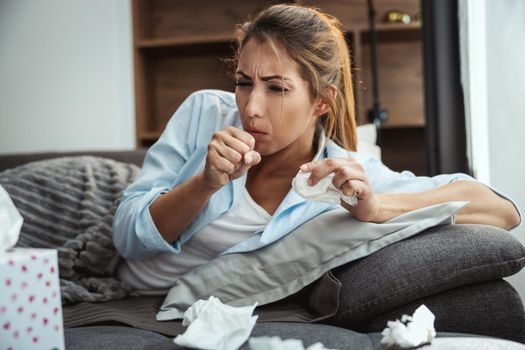 Young woman is lying sick at home couch coughing.