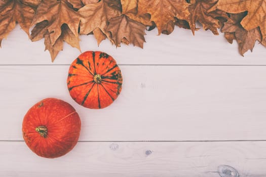 Image of pumpkins on wooden table with autumn leaves.Image is intentionally toned.