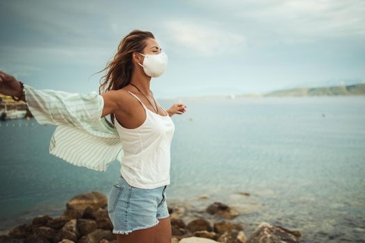 Shot of a relaxed young woman with protective N95 mask enjoying on the beach during the COVID-19.