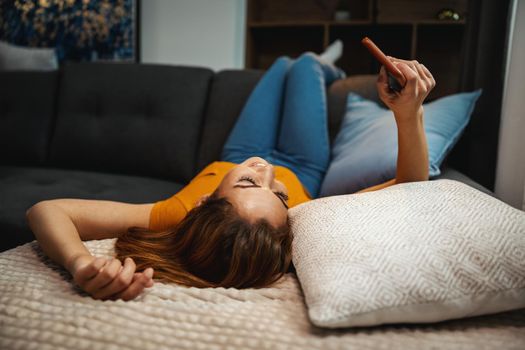 Attractive young woman lying on the sofa and using smartphone to surfing sthe net at home.