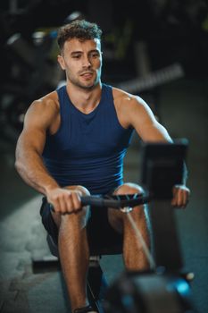 A young muscular man is pulling the row machine on crossfit training in the gym.