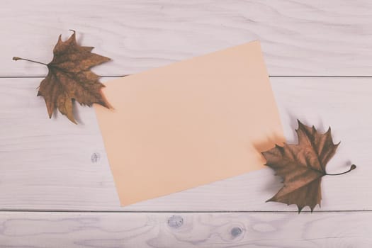 Empty pink paper on wooden table with autumn leaves.Image is intentionally toned