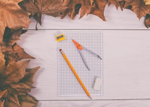 Empty white paper and school supplies on wooden table with autumn leaves.Toned image.