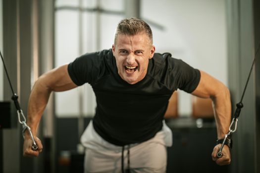 Muscular young man doing hard exercises for chest on cable machine during a strength training workout at the gym.
