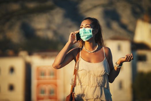 Shot of an attractive young woman wearing a surgical mask and using a smartphone while exploring the wonderful city of Meditteranian.
