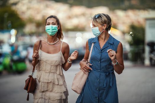 Shot of two attractive female friends who wear a surgical mask while exploring the wonderful city of Meditteranian.