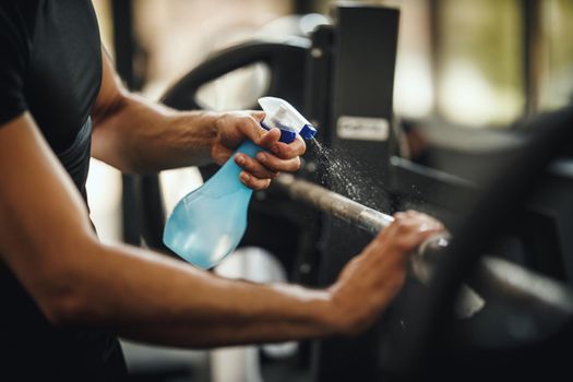 Shot of a muscular unrecognizable man cleaning fitness gym equipment before workout during Covid-19 pandemic.