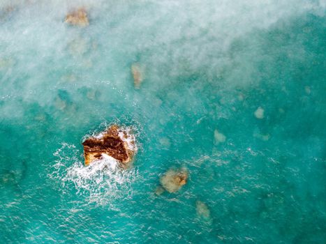 Aerial view from drone of the beautiful crystal clear turquoise and blue sea water, surrounding rocks and waves reaching sandy beach. 