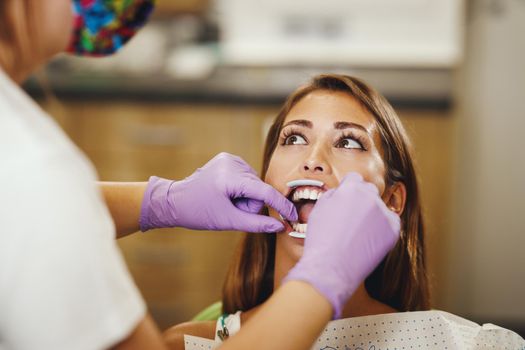 Shot of a beautiful young woman is at the dentist. She sits in the dentist's chair and the dentist preparing to sets braces on her teeth putting aesthetic self-aligning lingual locks.