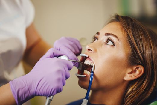Shot of a beautiful young woman is at the dentist. She sits in the dentist's chair and the dentist preparing to sets braces on her teeth putting aesthetic self-aligning lingual locks.