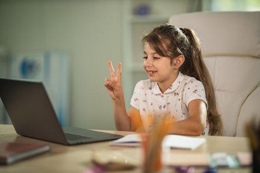 Shot of a diligent little girl using laptop to do a online lesson at home during COVID-19 pandemic.