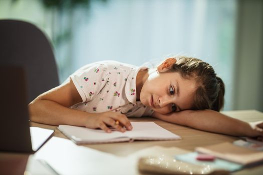 Shot of a tired little girl using laptop to do a online lesson at home during COVID-19 pandemic.