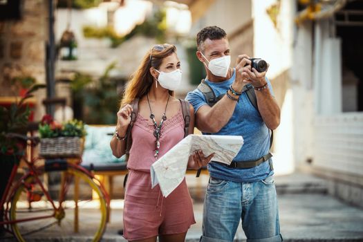 Shot of a happy couple with protective N95 mask spending time on vacation and exploring a Mediterranean city at corona pandemic. 