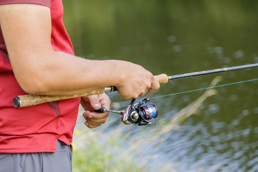 A man with a beard is fishing on the river. A fisherman with a fishing rod is fishing on the river bank.