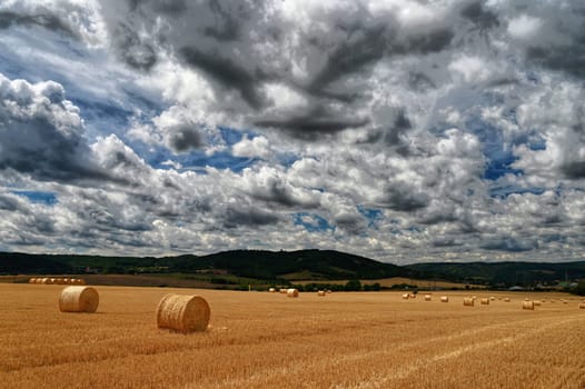 Hay bail harvesting in golden field landscape. Summer Farm Scenery with Haystack on the Background of Beautiful Sunset.