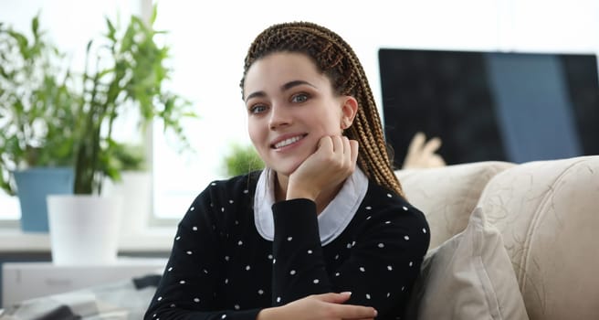 Portrait of young beautiful woman looking happy and smiling in living room indoors. Charming female posing on camera in black polka dot sweater. Spare leisure time concept