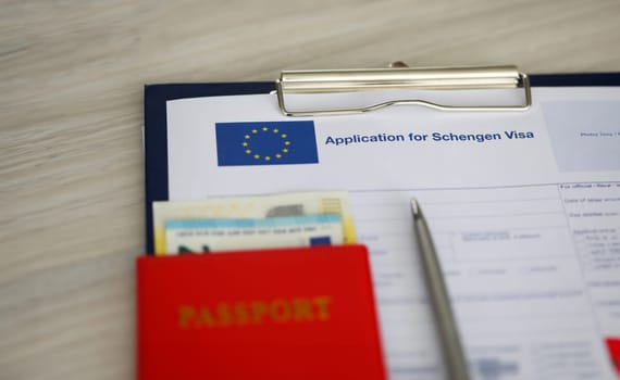Close-up of clipboard with application for schengen visa document and passport with banknotes. Paper for applying to entry in european union. Travelling abroad concept