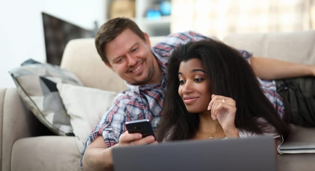 Portrait of man showing something interesting to woman in smartphone. Surprised female smiling. Couple spending time together. Mixed race and entertainment concept