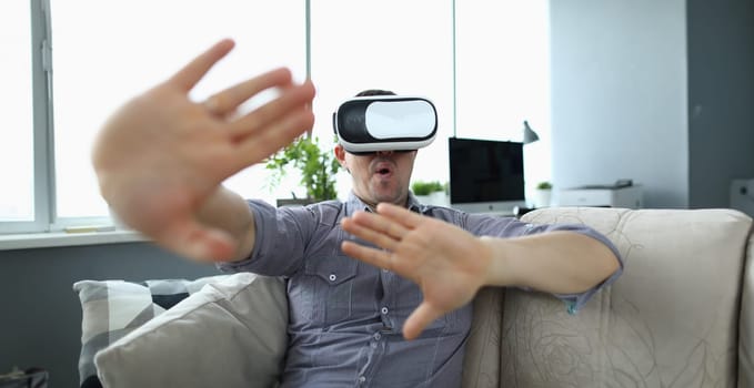 Close-up view of young man watching realistic picture in virtual reality headset. Shocked male having fun at home. Technology and entertainment concept