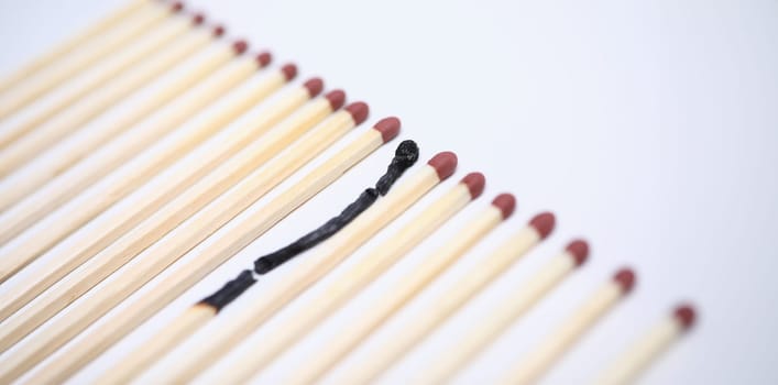 Close-up view of one wooden burnt match among many new whole. Conceptual image of non-renewable energy. Burn out syndrome and stress concept. Isolated on white background