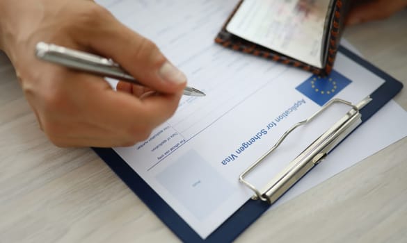 Close-up of persons hand holding silver pen and filling application for schengen visa. Essential step to entry in european union. Eu and travelling abroad concept