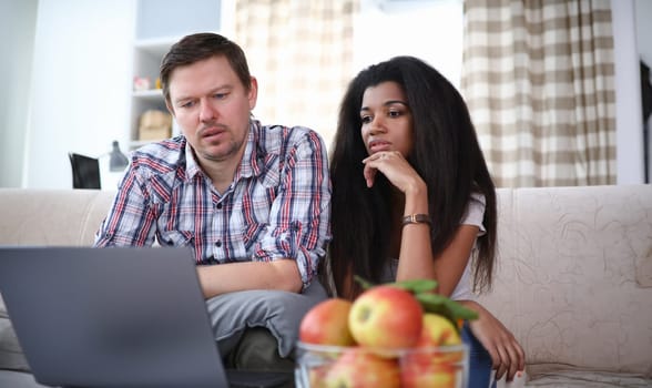 Portrait of concentrated family surfing something via internet app on laptop. Man and woman sitting in comfortable room. People looking at screen seriously