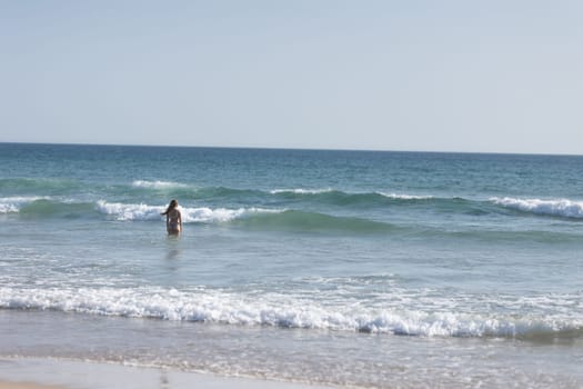 A young woman with nice body standing in the ocean - back view. Mid shot