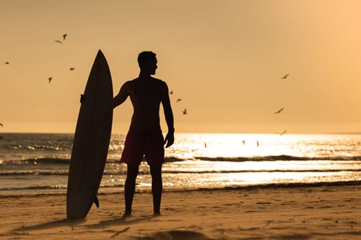 Silhouette of a pumped-up sports surfer man on the beach during sunset. Mid shot