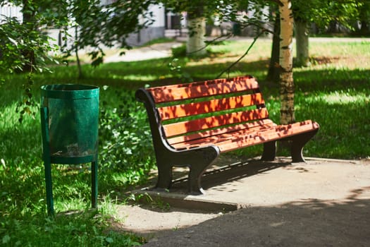 Photo of bench and green trash can in city park. Caring for environment. Clean streets without garbage.
